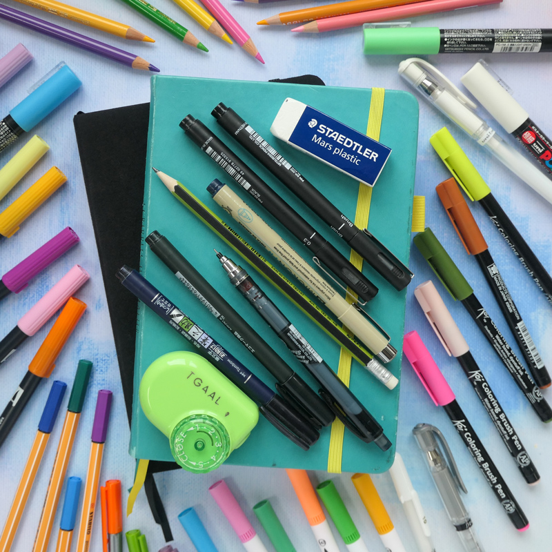 selection of pens and pencils surrounding two bullet journal notebooks