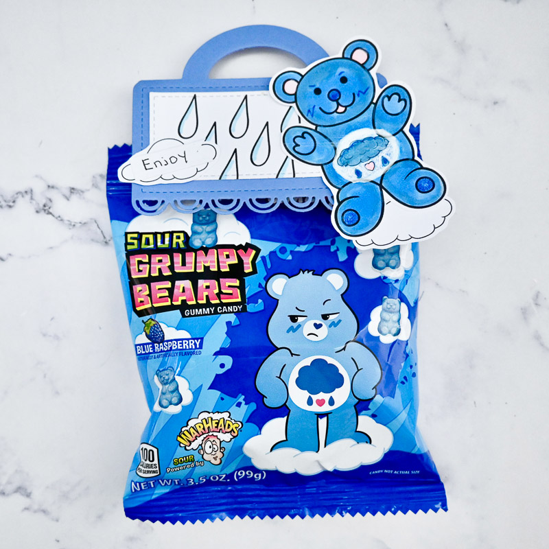 packet of grumpy bears candy with a handmade topper attached featuring a hand coloured bear and raindrops set on a marble tabletop